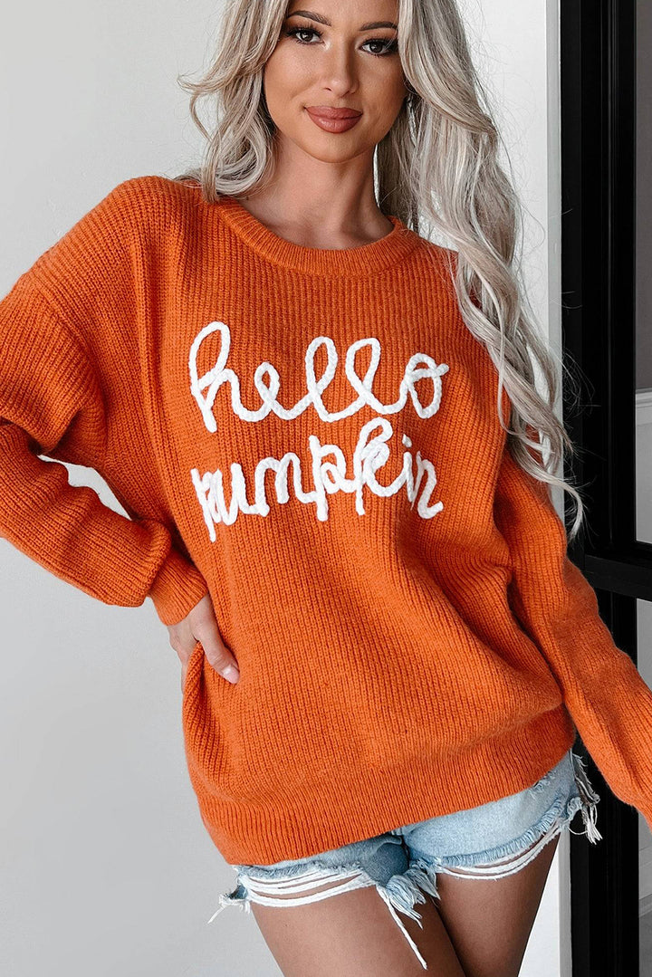 Flamingo Hello Pumpkin Graphic Sweater, featuring white hello pumpkin text, paired with distressed denim shorts. She stands indoors, smiling slightly with one hand on her hip.