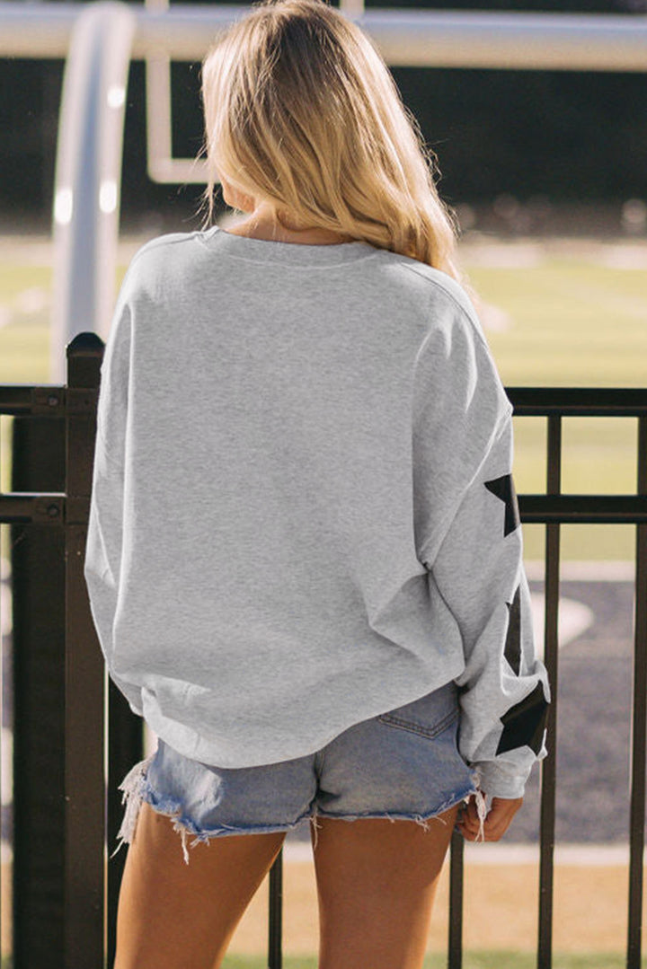 Black Game Day Graphic Rugby Football Season Sweatshirt and frayed denim shorts, facing away by a black metal fence.