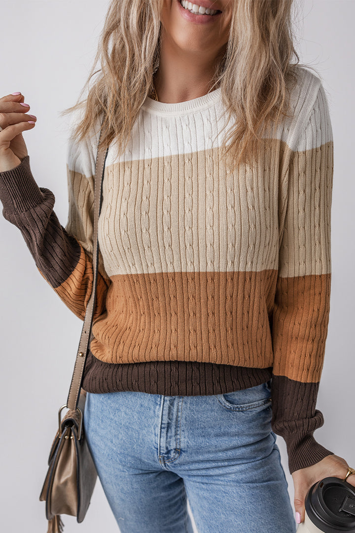 Khaki Colorblock Cable Knit Round Neck Sweater, featuring white, beige, tan, and brown stripes. She pairs it with light blue jeans, carrying a crossbody purse and coffee cup as her wavy hair partially covers her smiling face.